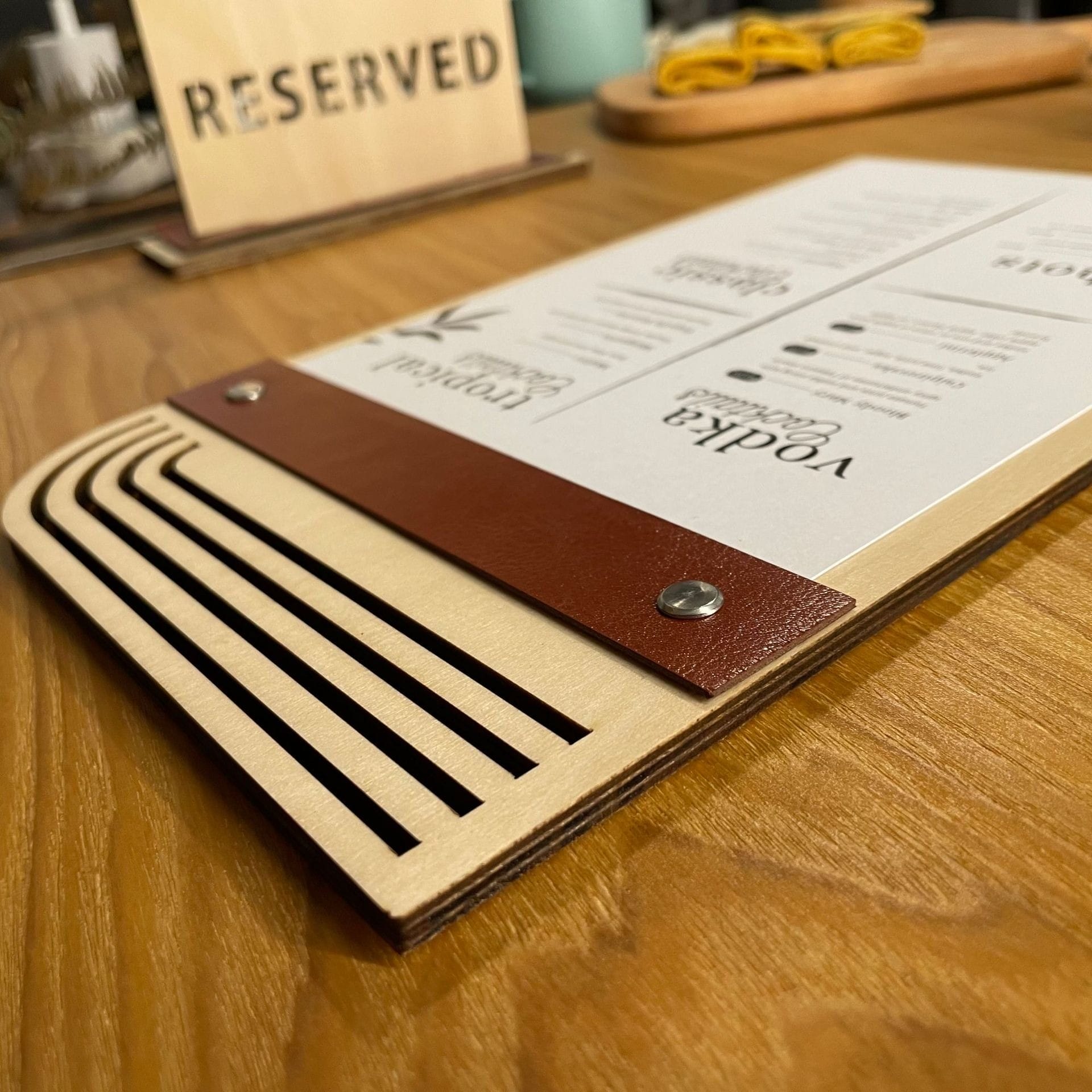 Wooden menu board with brown leather insert, showing Vodka and Tropical cocktails. Eco-friendly design.