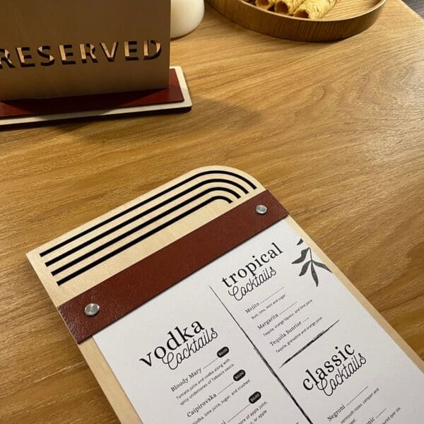 Wooden menu board with leather strap, showcasing cocktail list. Eco-friendly design with replaceable inserts.
