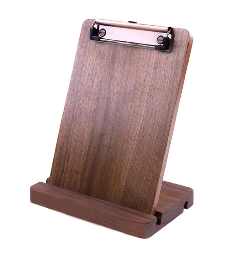 Wooden clipboard with rose gold clip, angled on a stand.