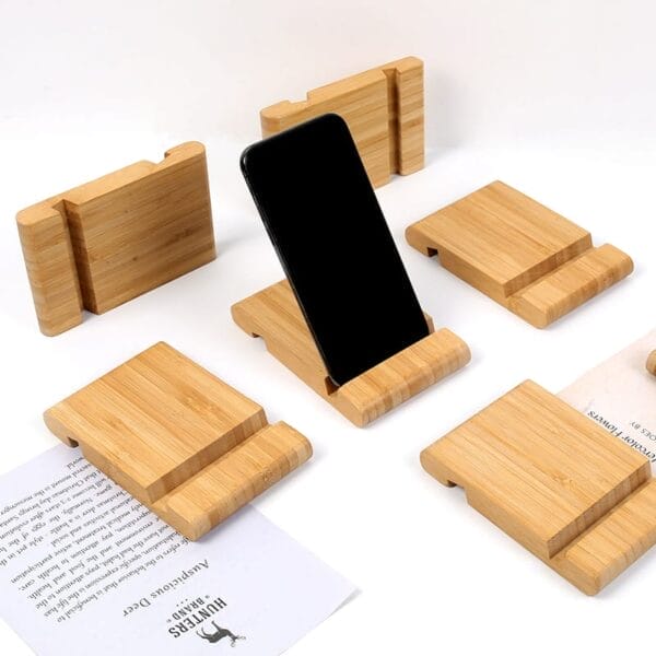 A black smartphone is displayed on a wooden phone holder, surrounded by five similar holders, with a paper partially visible on the left side.