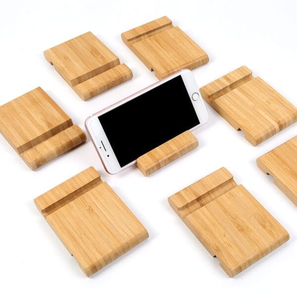 A white smartphone is propped up on an adjustable wooden phone holder, surrounded by several identical bamboo brackets arranged neatly on a white surface.