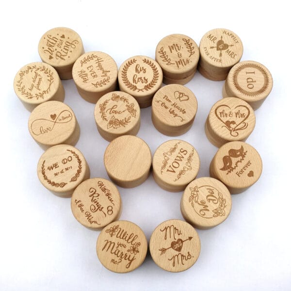 Wooden tokens engraved with romantic phrases and wedding-themed designs are arranged in a heart shape on a white background, perfect for displaying near wedding rings or inside a customizable wooden ring box.