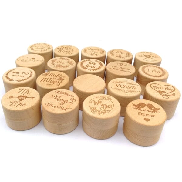 A group of small, round wooden ring boxes with wedding-themed engravings such as “We Do!”, “Forever,” “I do,” and “Mr & Mrs” displayed on the lids, perfect for presenting wedding rings in customizable packaging.