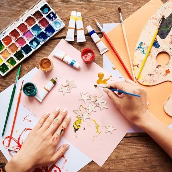 Hands painting wooden star shapes with acrylic paints and brushes. Wholesale craft supplies.