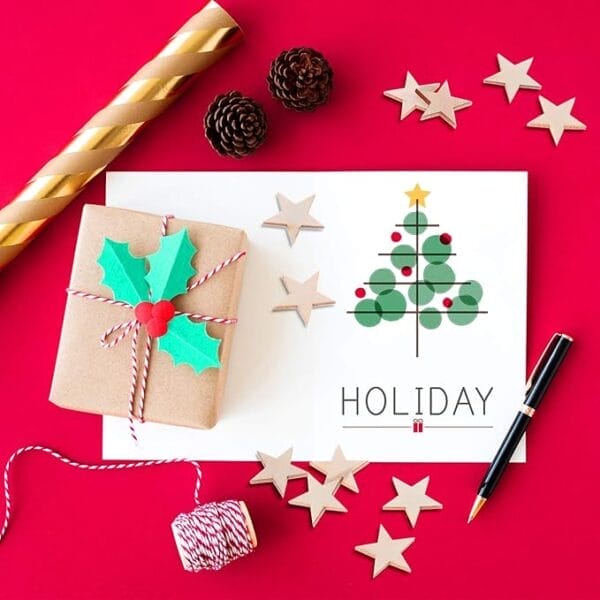 Flatlay of Christmas gift, card with illustrated tree, wooden stars, and craft supplies. Holiday craft supplies.