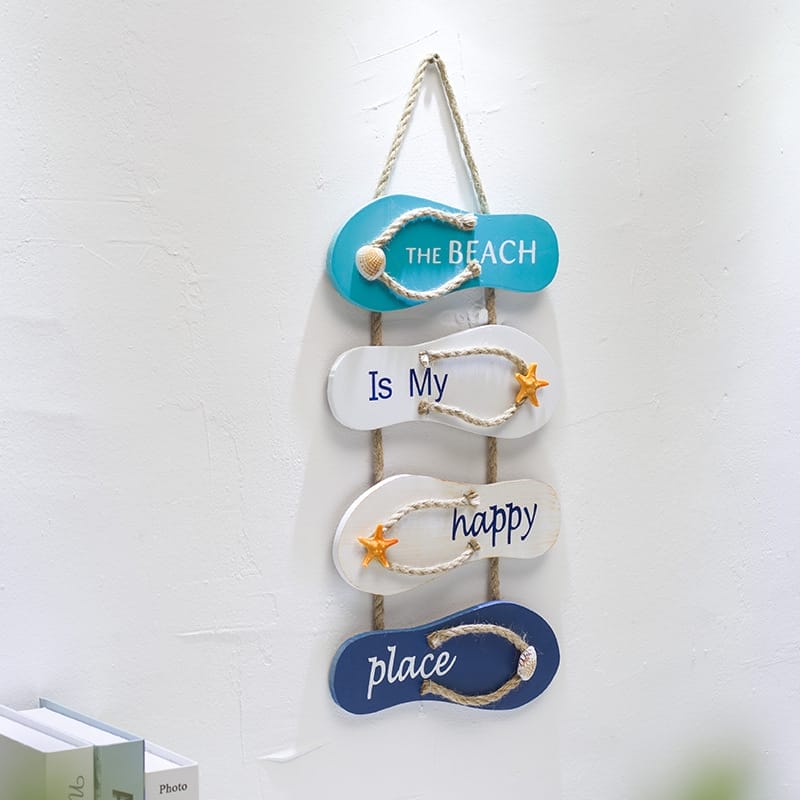 A wall hanging made of four flip-flops reads "The Beach Is My Happy Place," decorated with rope, a shell, starfish accents, and styled to resemble charming wooden signs.