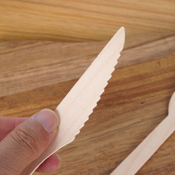 Close-up of a hand holding a wooden butter knife, part of a wholesale set of disposable wooden cutlery.