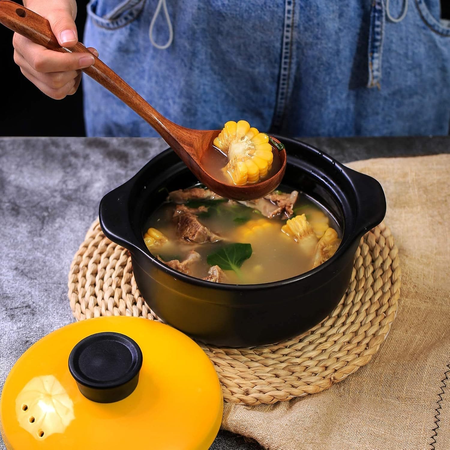 Person using a wooden spoon to serve corn soup from a black pot.