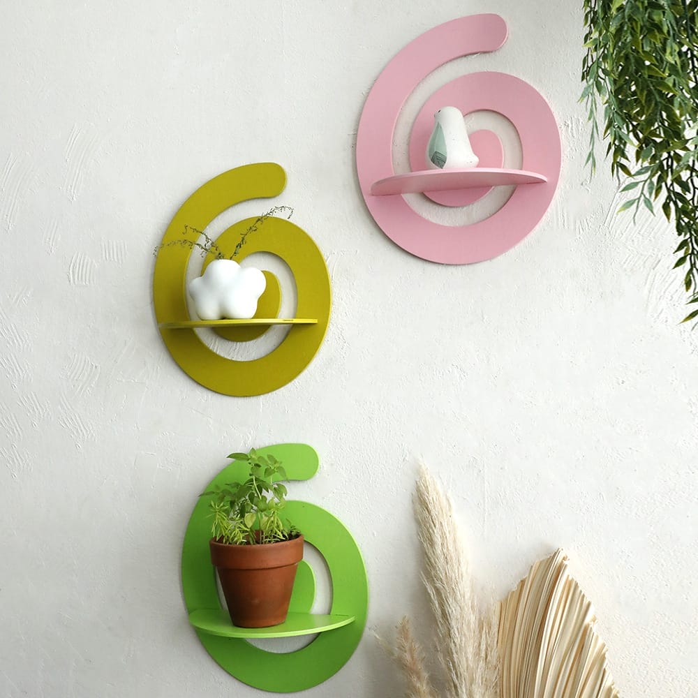 Three irregular shape wall shelves, designed like the number six, are mounted on a white wall—each holding small decorative items and a potted plant.