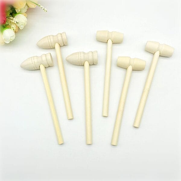 Six small, light-colored mini wooden hammer toys with round handles are arranged on a white surface; ideal for wooden sticks crafts, two feature pointed heads while four have cylindrical heads with central grooves. Perfect for wholesale orders.