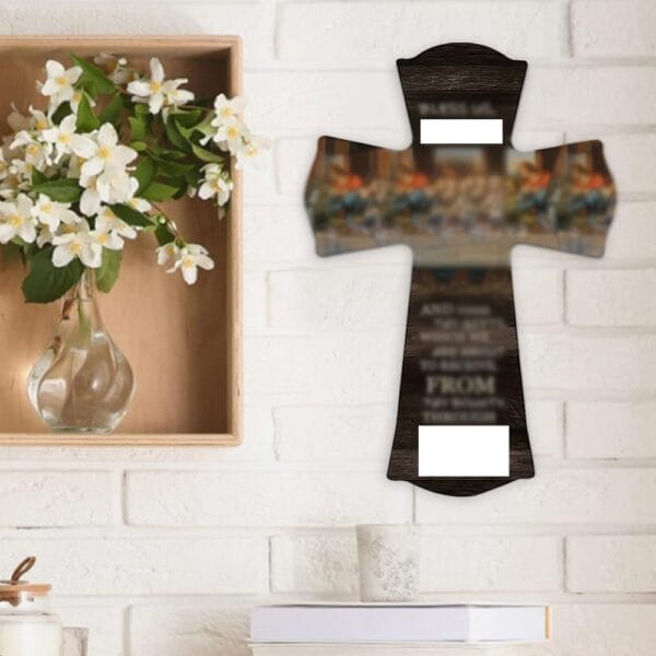 A wooden wall cross with a blurred image and text hangs on a white brick wall next to a vase of white flowers, showcasing eco-friendly craftsmanship from a wholesale manufacturer.
