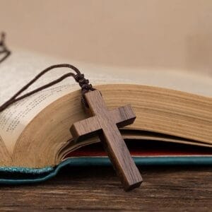 Small wooden cross necklace on open book. Eco-friendly Easter & home decor from manufacturer.