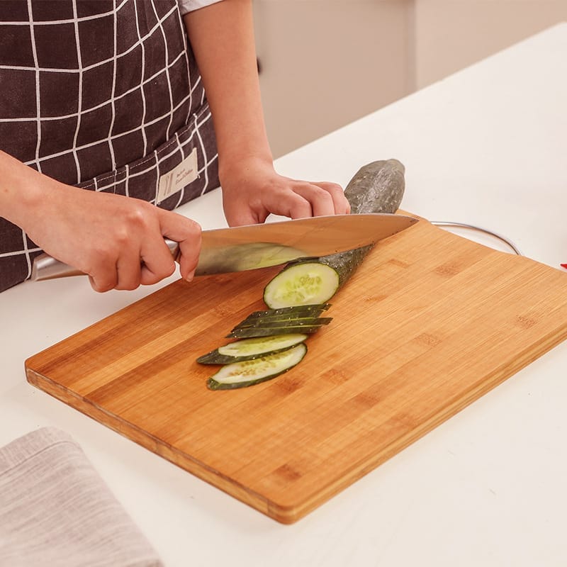 Person slicing cucumbers on a large, rectangular bamboo cutting board. High-quality solid bamboo cutting board.