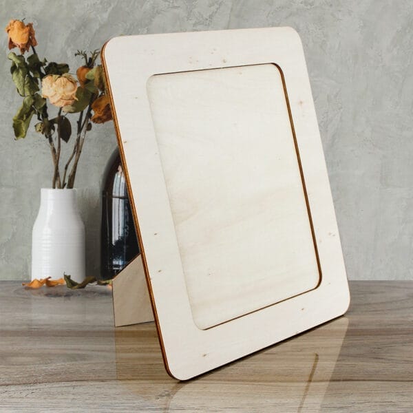 Blank wooden photo frame on a table beside dried flowers in a white vase