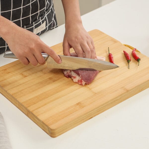 Person slicing meat on a large, eco-friendly bamboo cutting board. Wholesale bamboo cutting boards available.
