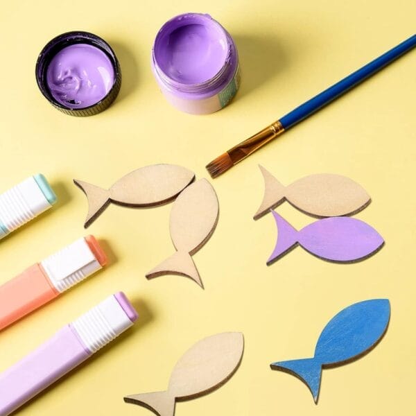 Wooden fish shapes, paint, and markers ready for a craft project. Customizable wood pieces for decoration.
