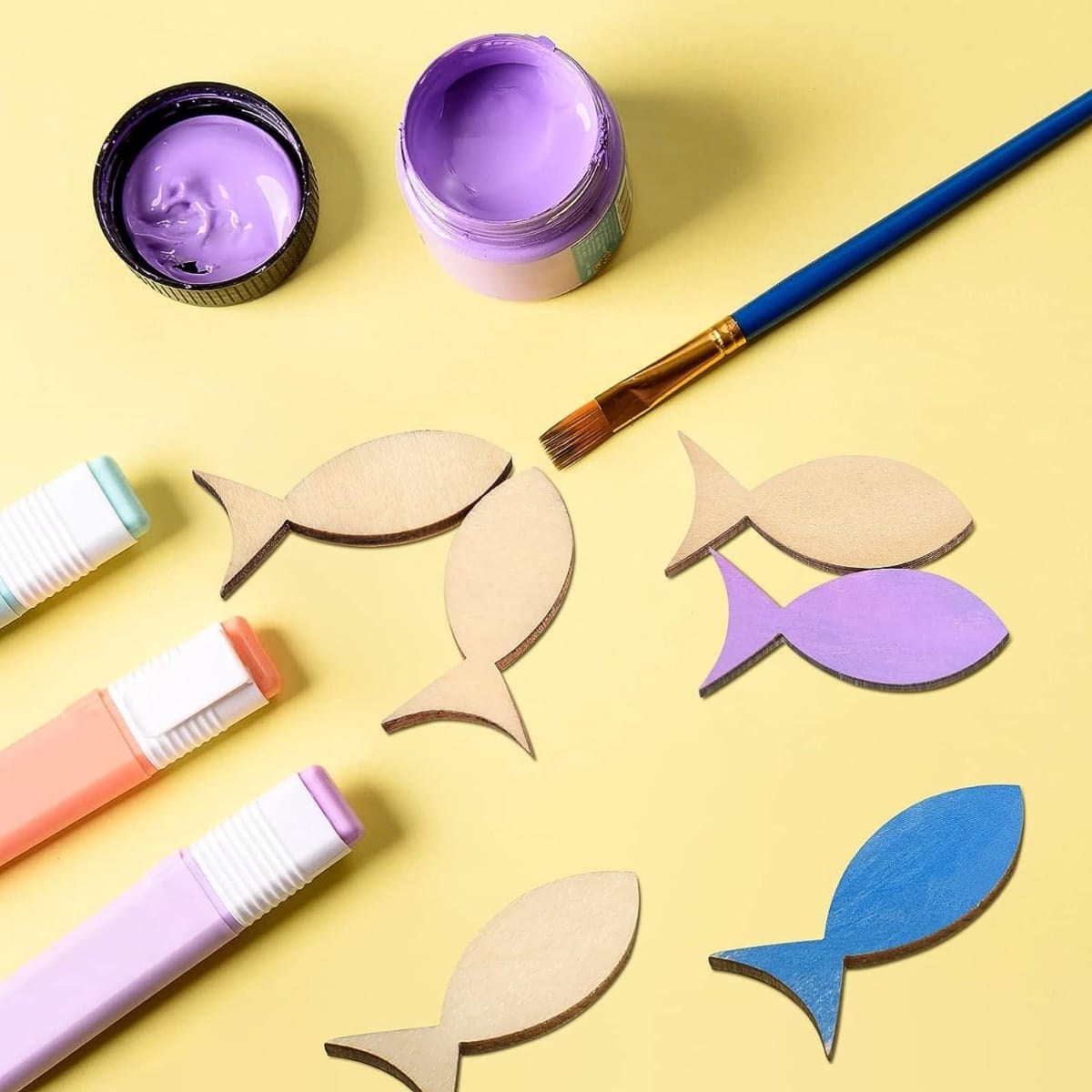 Wooden fish shapes, paint, and markers ready for a craft project. Customizable wood pieces for decoration.