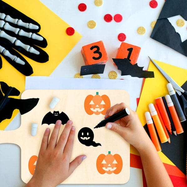 Child's hands painting Halloween-themed wooden cutouts. DIY pumpkin and bat designs.