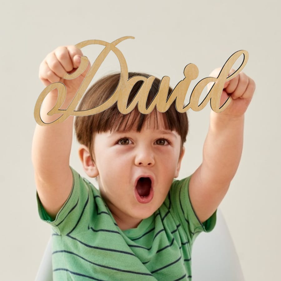 Happy toddler holding a custom wood name signs that says "David".