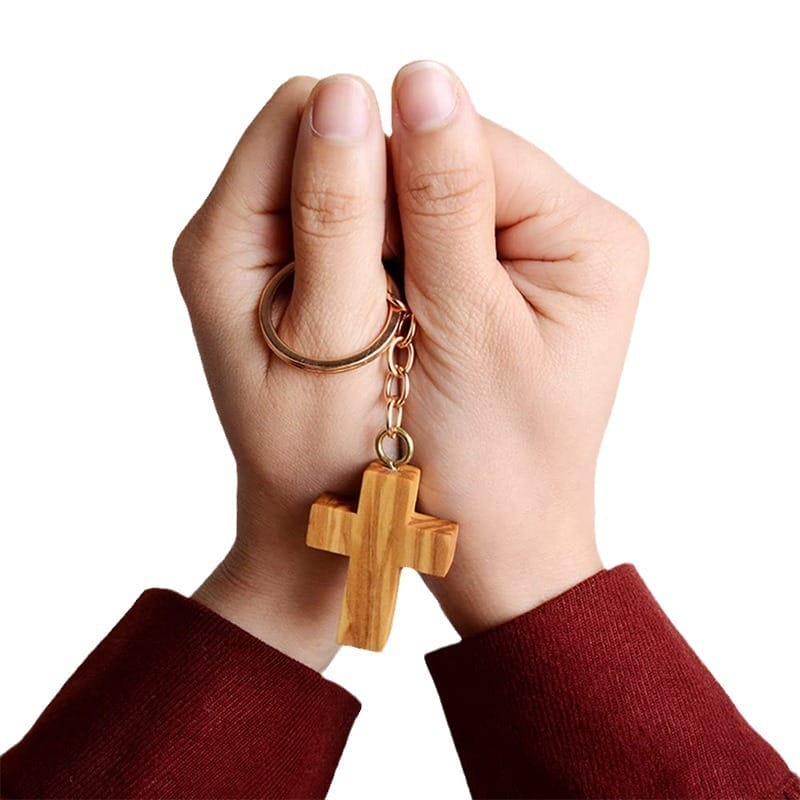 Custom wooden keychain hands holding a wooden olive wood cross keychain. Wholesale supplier of custom wooden keychains.