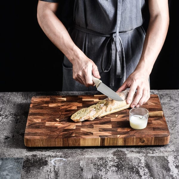 Chef slicing baguette on a double-sided, factory custom end grain cutting board.