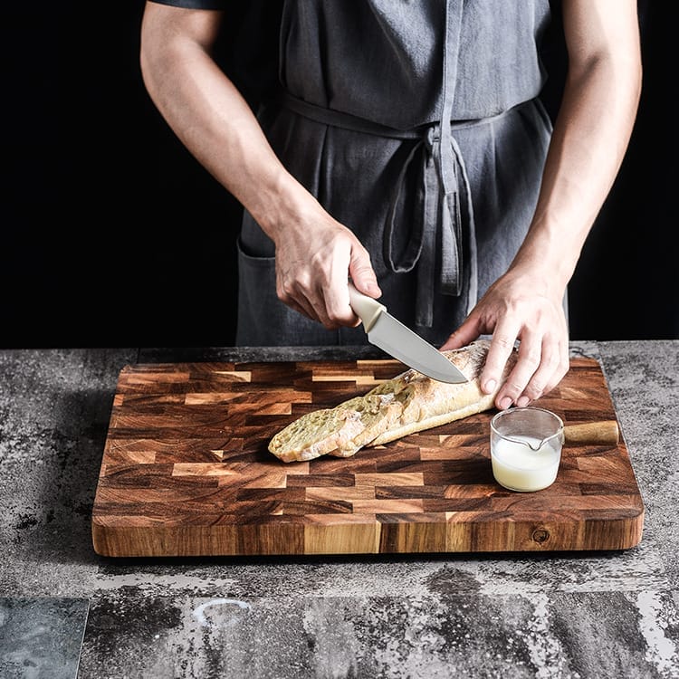 Chef slicing baguette on a double-sided, factory custom end grain cutting board.