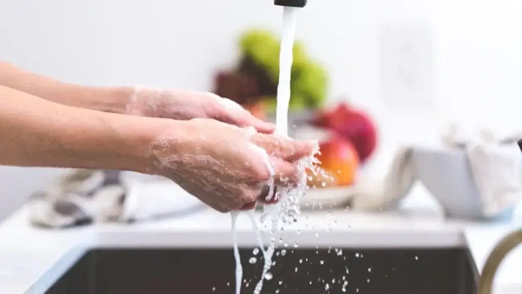Person washing hands thoroughly with soap and water under a faucet.