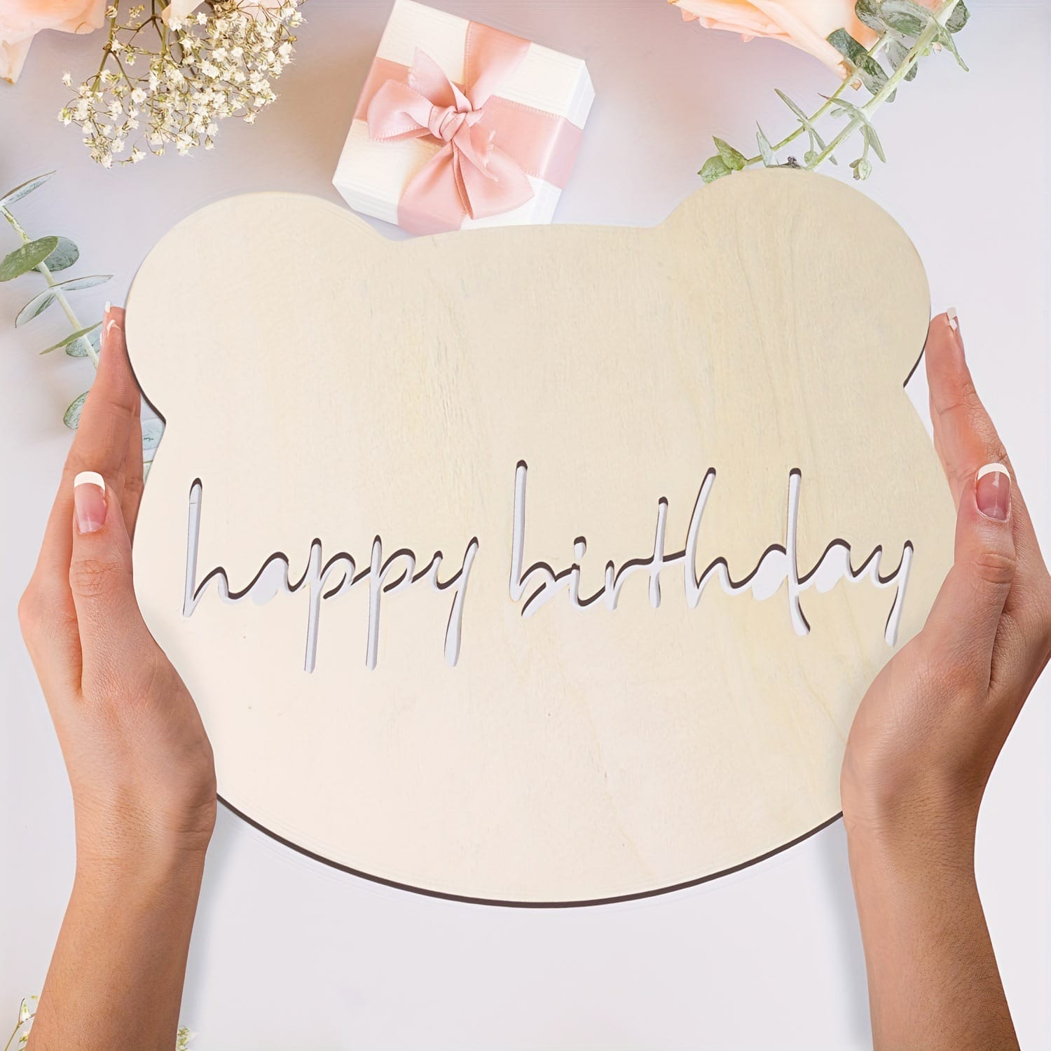Hands holding a wooden bear-shaped "Happy Birthday" cutout. Laser cut wood decoration.