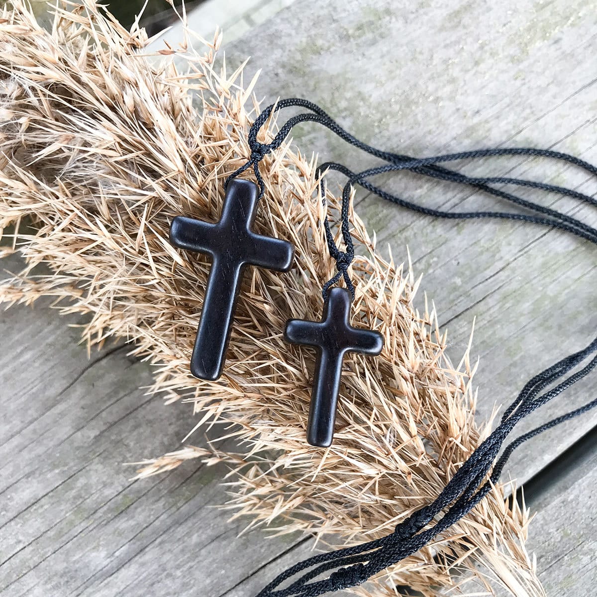Men's eco-friendly wooden cross necklace pendant set. Two black wooden crosses on natural fiber background.