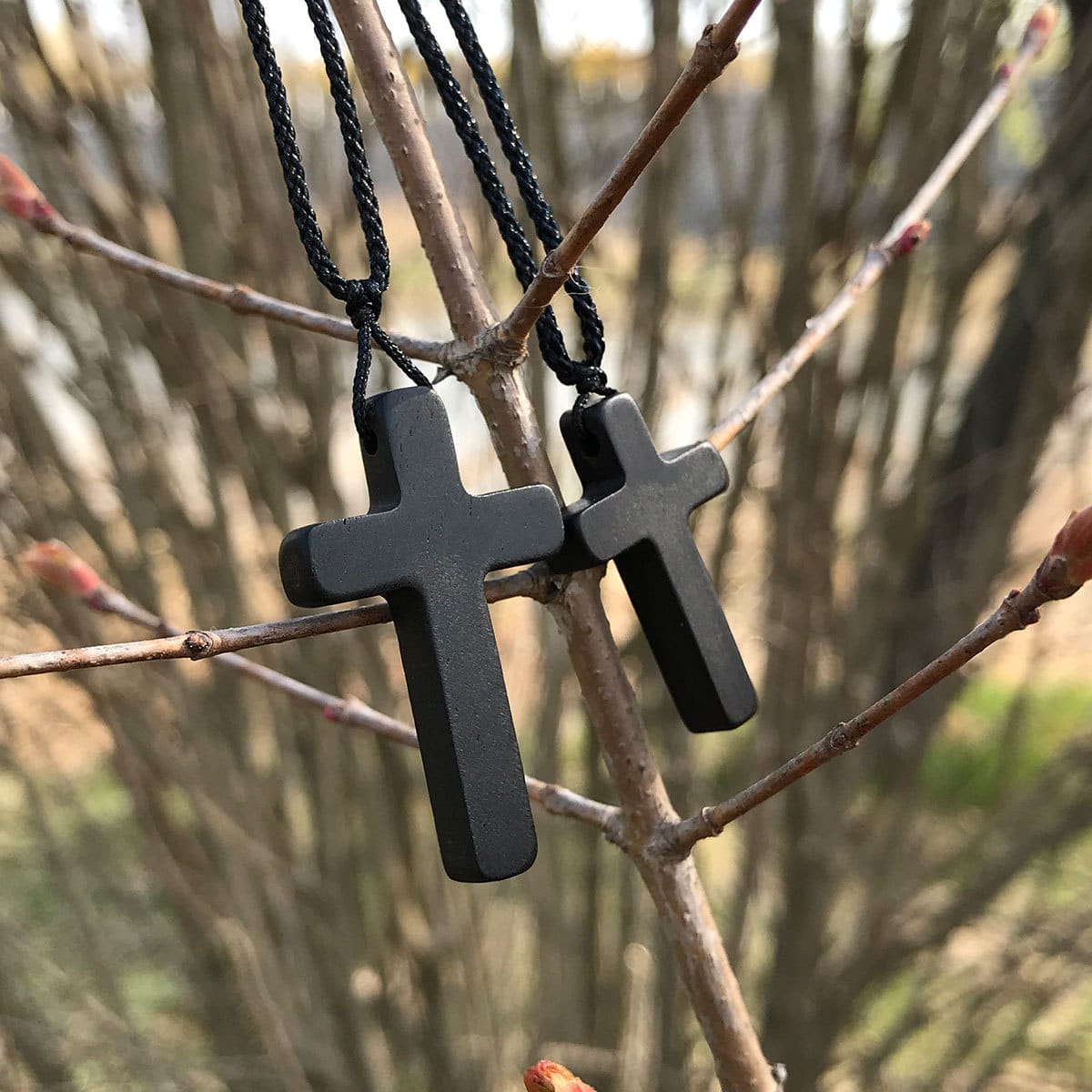 Men's eco-friendly wooden cross necklace pendant. Two black wooden cross necklaces hanging on a tree branch.