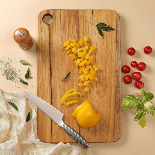Wooden cutting board with chopped yellow bell peppers, knife, and herbs. Non toxic wood cutting board