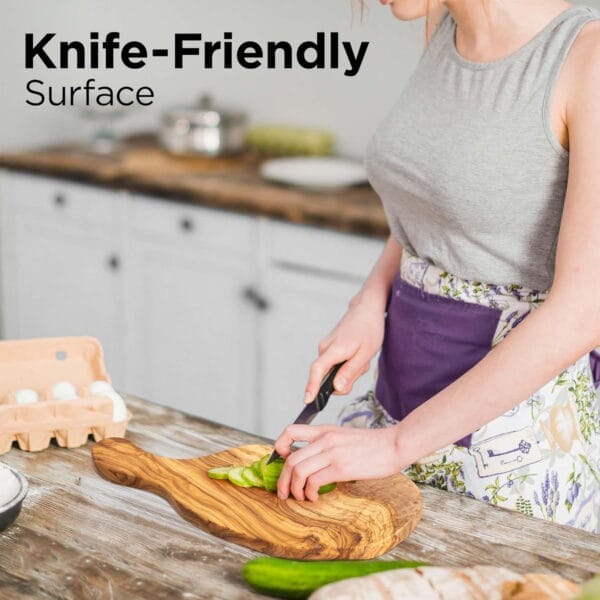 Woman using a large olive wood cutting board to slice cucumbers. Eco-friendly kitchen.