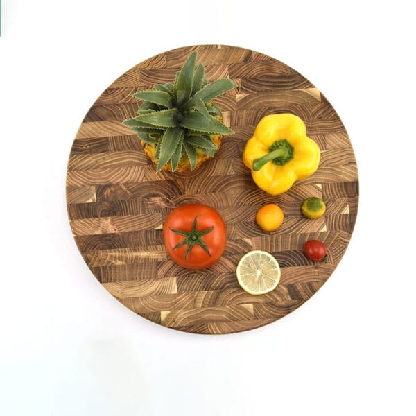 Round teak end-grain cutting board with assorted fruits and vegetables. Wholesale wood chopping board.