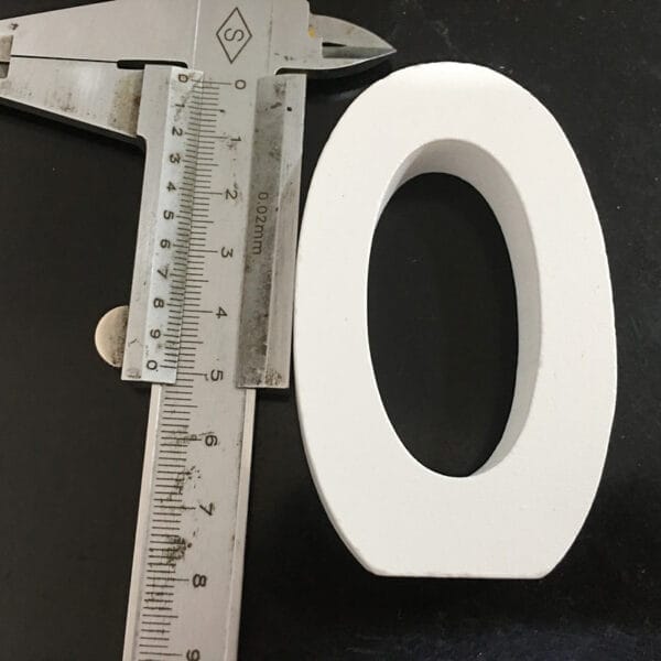 Close-up of white wooden letter O, measured with calipers. Modern minimalist home decor.