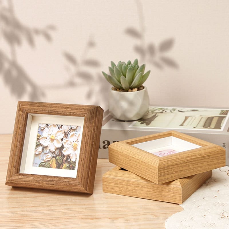 Square wooden picture frames with floral art on a table next to a small plant