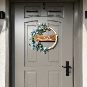 Wooden bead wreath with "hello" sign on gray door. Supplier of wooden bead door hangings.