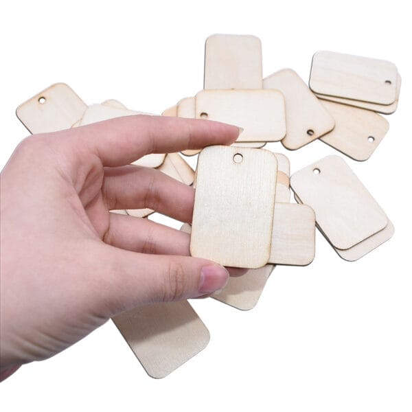 Hand holding blank rectangular wooden tags; ideal for crafts and wholesale.