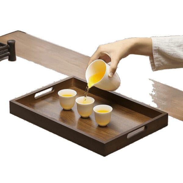 Person pouring tea into small cups on a dark brown wooden serving tray. Eco-friendly wooden tray.