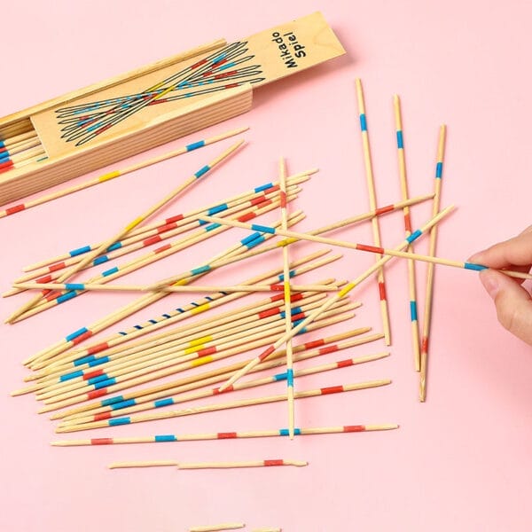 Colorful wooden pick-up sticks scattered on a pink background, next to their wooden box. A hand picks up a stick.