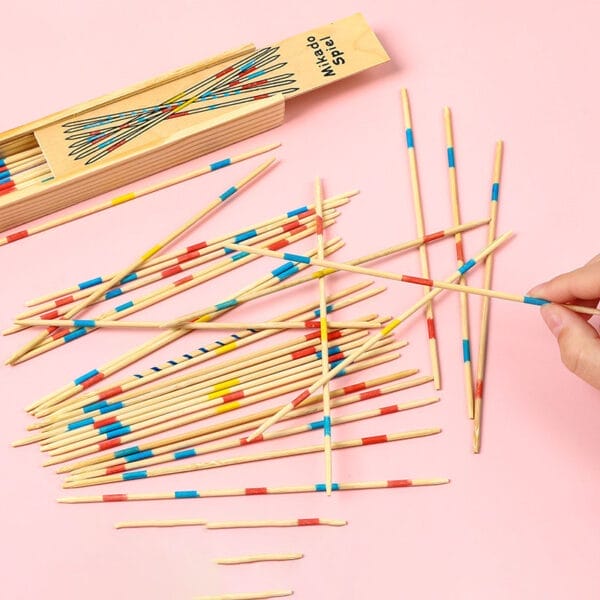 Colorful wooden pick-up sticks scattered on a pink background, next to their wooden box. A hand picks up a stick.