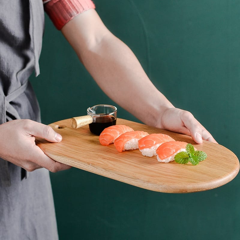 Person presenting sushi on a rectangular wooden cutting board.
