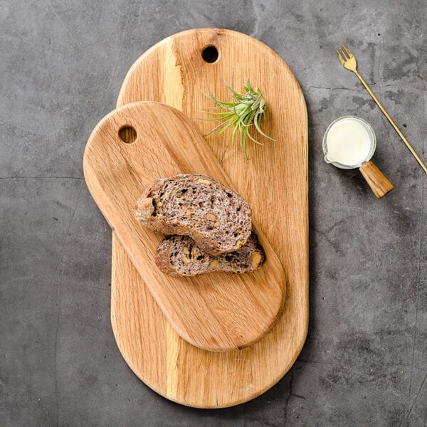 Two oval wooden bread boards, one smaller atop the larger, with sliced bread and a small plant.