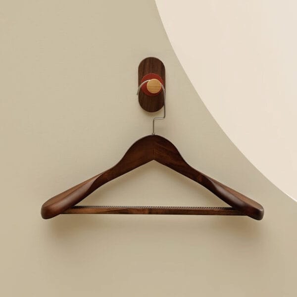Dark wood coat hanger on a wall-mounted hook. Custom wooden hangers available.
