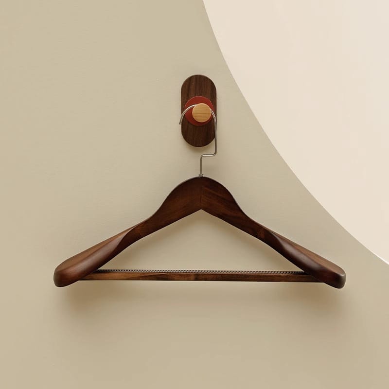 Dark wood coat hanger on a wall-mounted hook. Custom wooden hangers available.