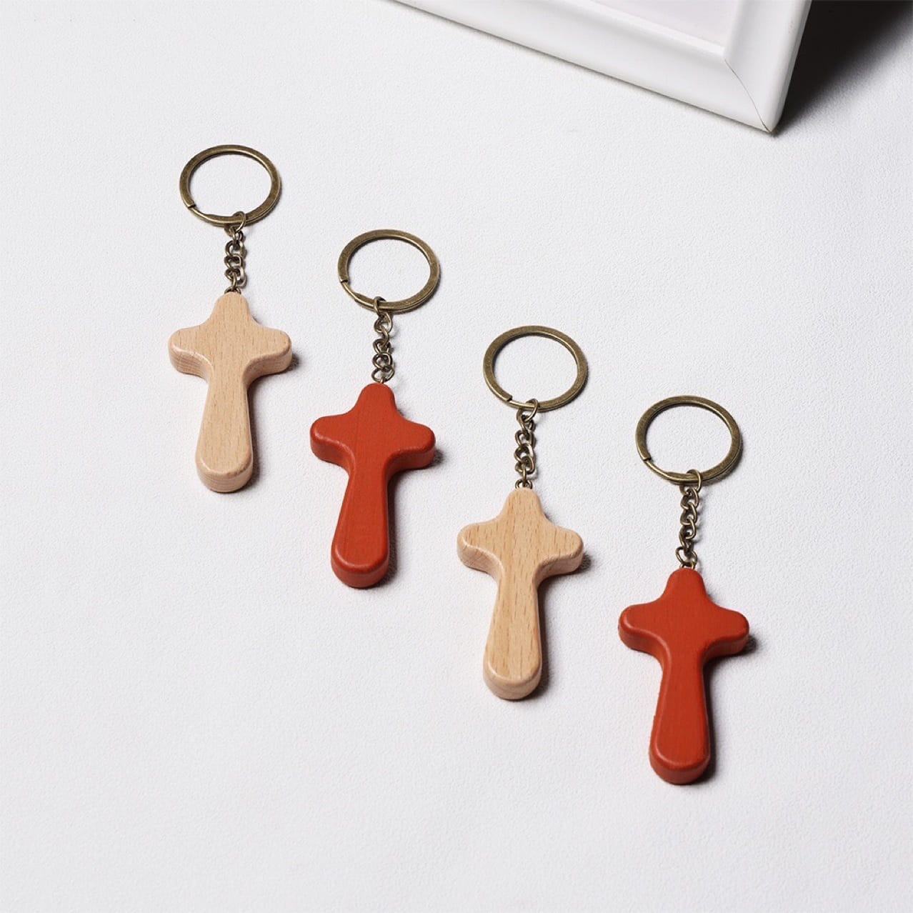 Four wooden cross keychains, two natural and two terracotta, displayed on a white surface. Custom wood cross keychains.