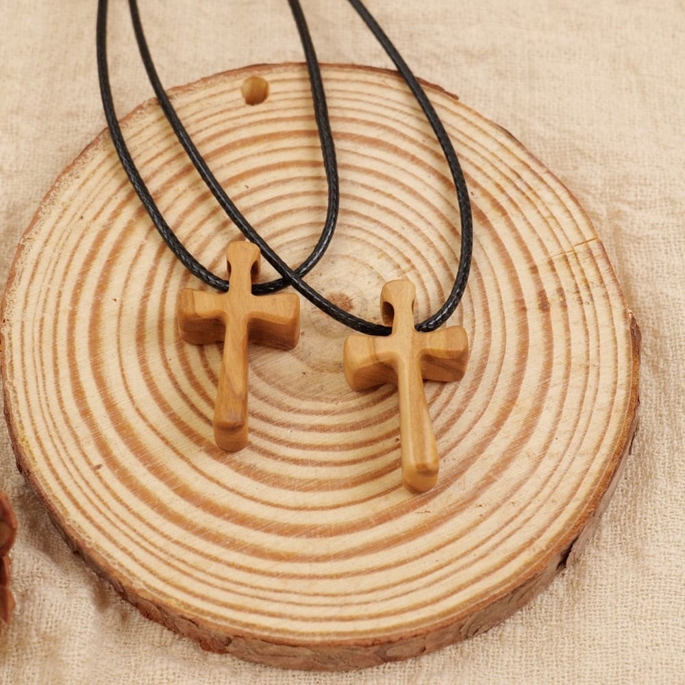 Olive wooden crucifix necklace: Two wooden crucifix necklaces with black cords, displayed on a circular wooden base.
