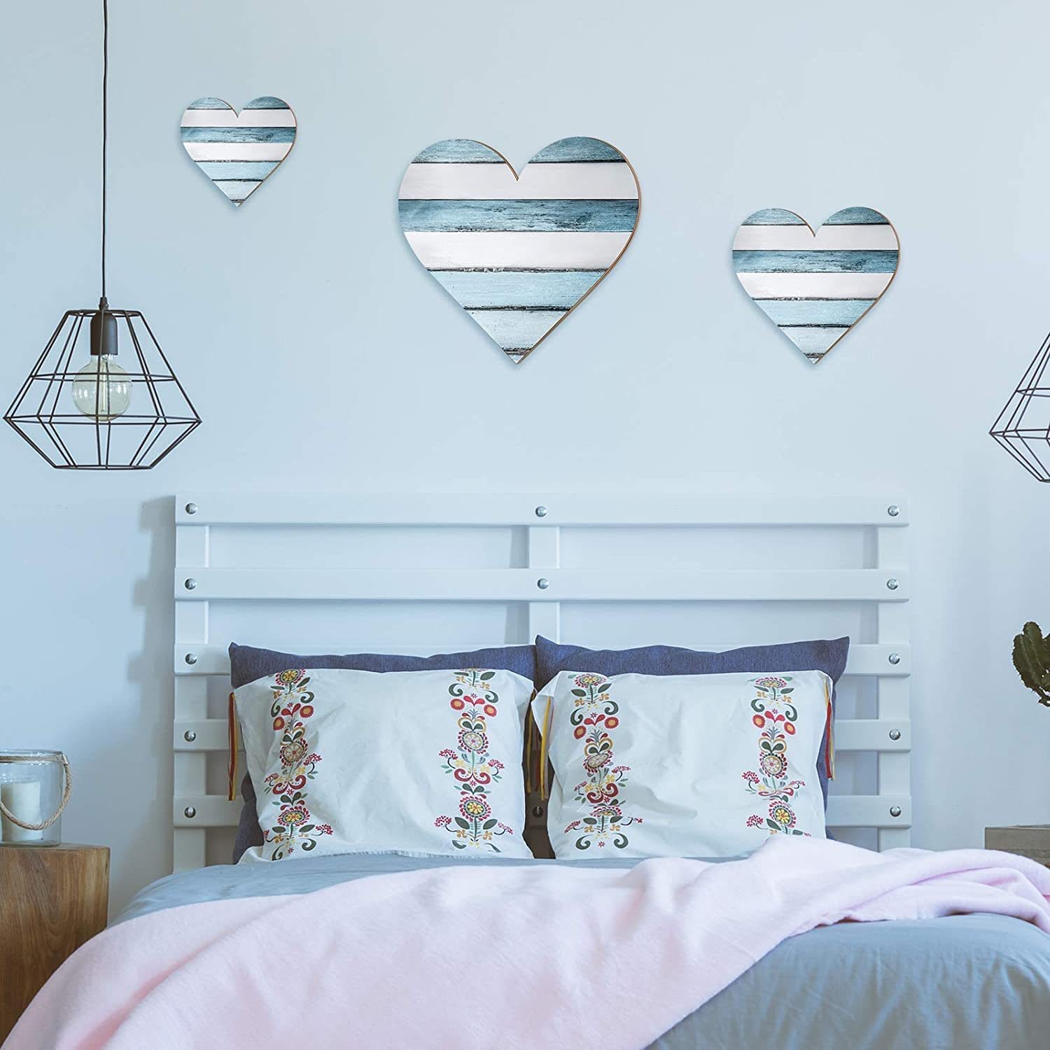Three rustic blue and white heart-shaped wooden wall decorations above a bed. Heart-shaped bedroom wall decor.