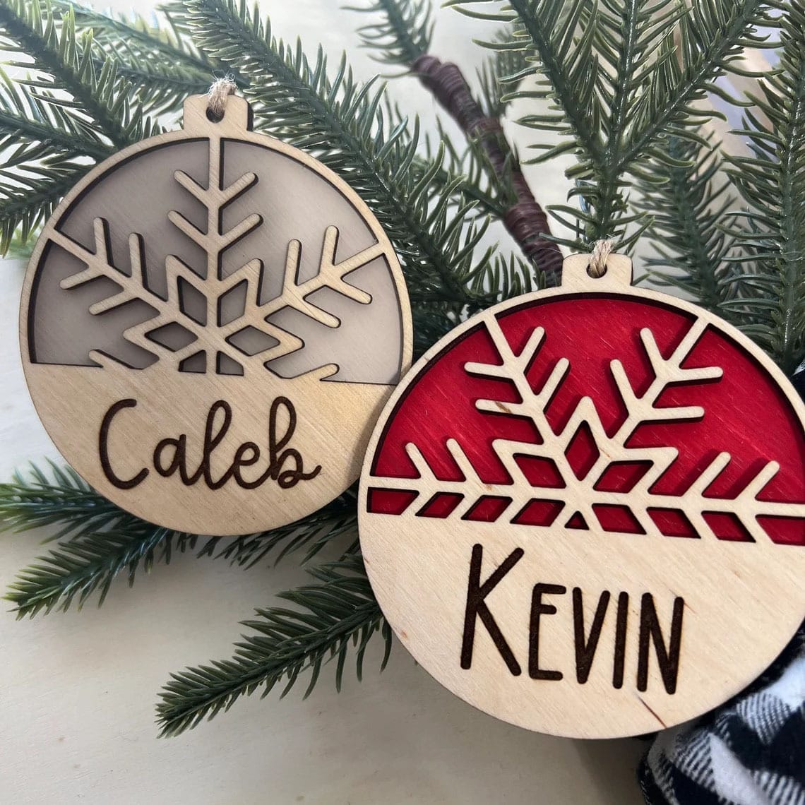 Two personalized wooden Christmas ornaments; one gray, one red, with snowflake designs and names Caleb & Kevin.