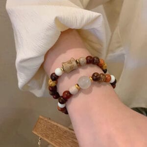 Woman's wrist wearing two beaded bracelets; one features a carved wooden charm.