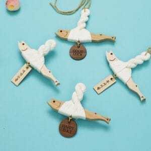 Four wooden fish ornaments wrapped in white yarn, each with a different good luck charm.